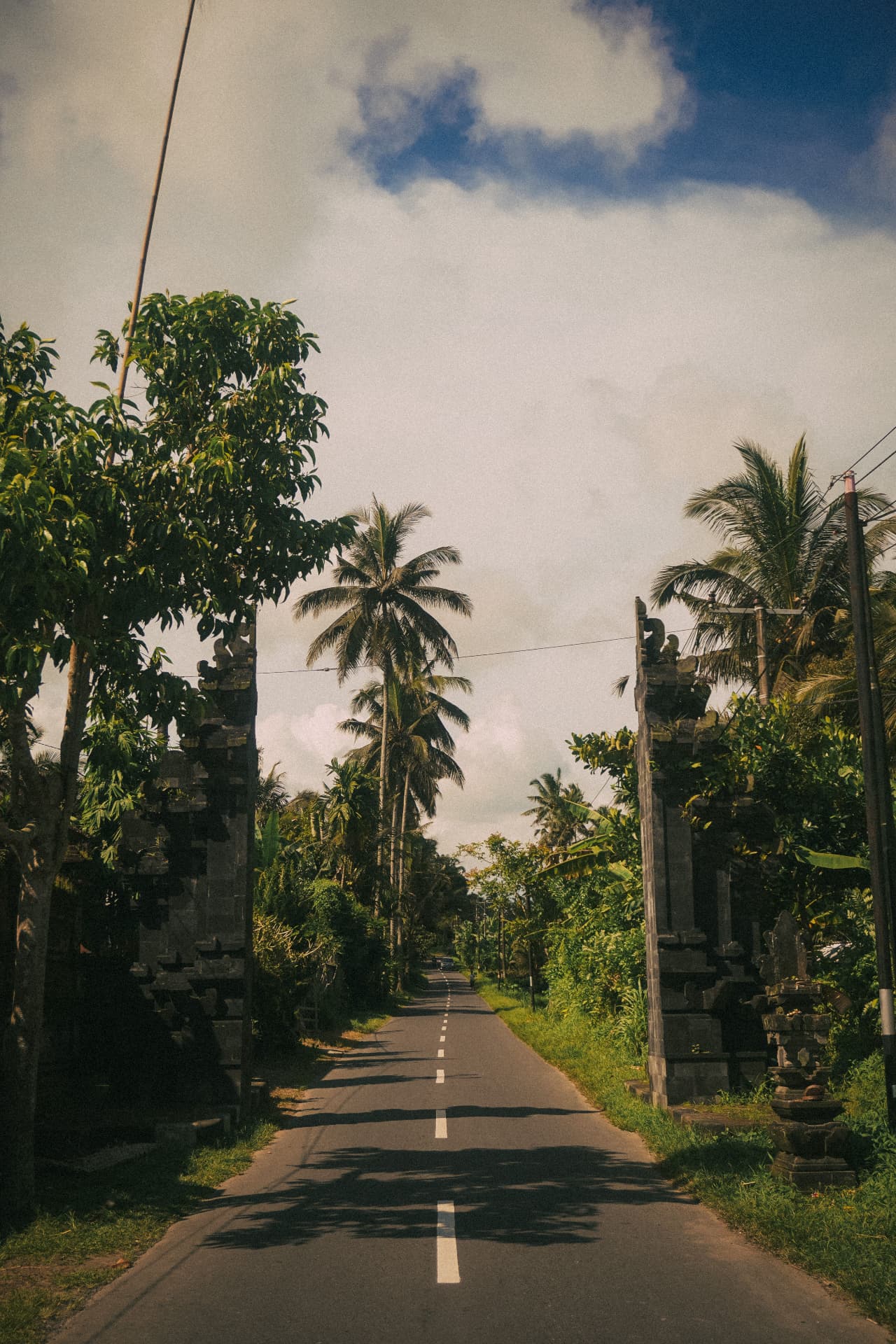 Palm lined village road running between traditional Balinese stone gates in Uluwatu