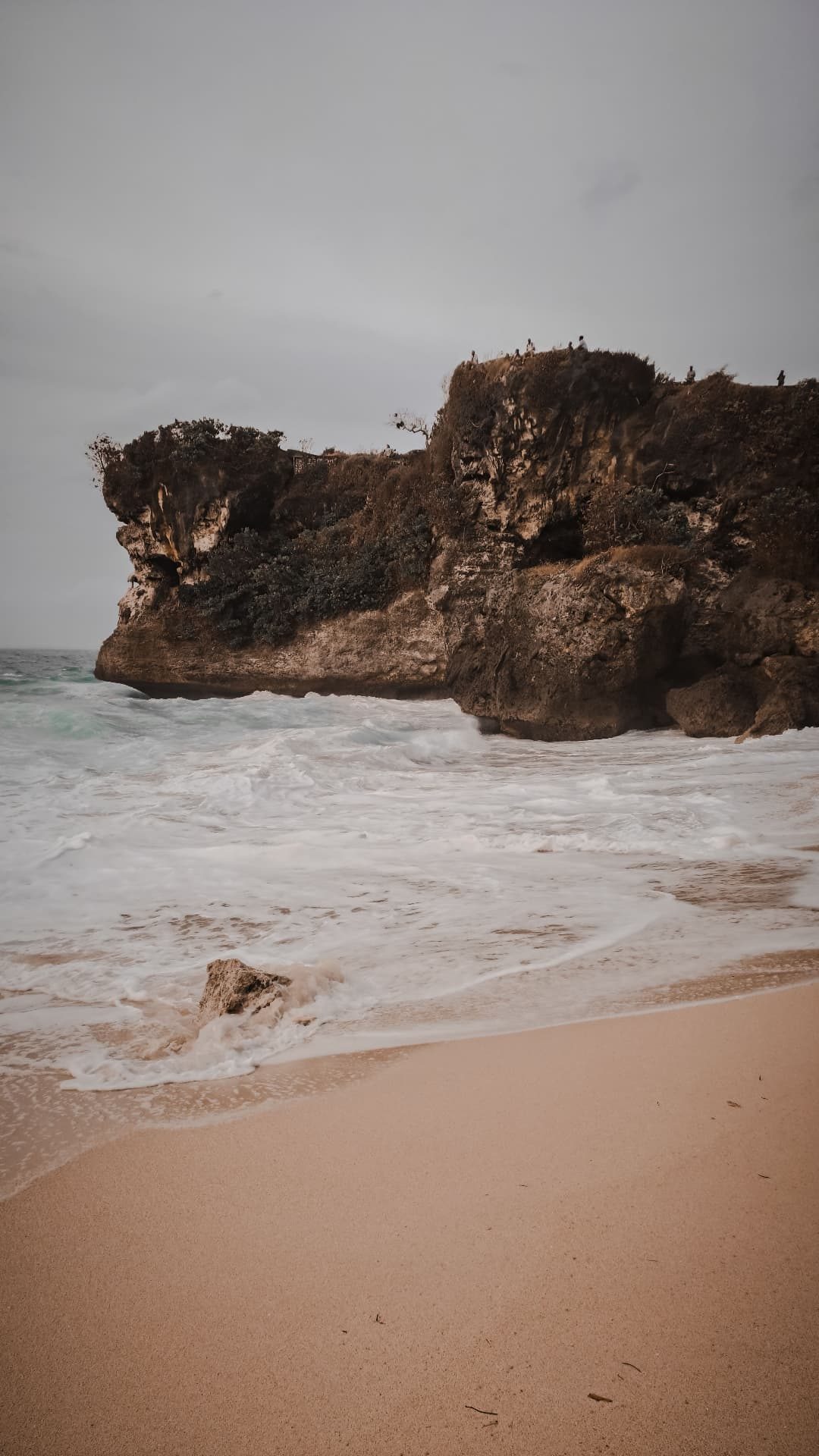 Waves washing the sand beneath an Uluwatu cliff on a moody day