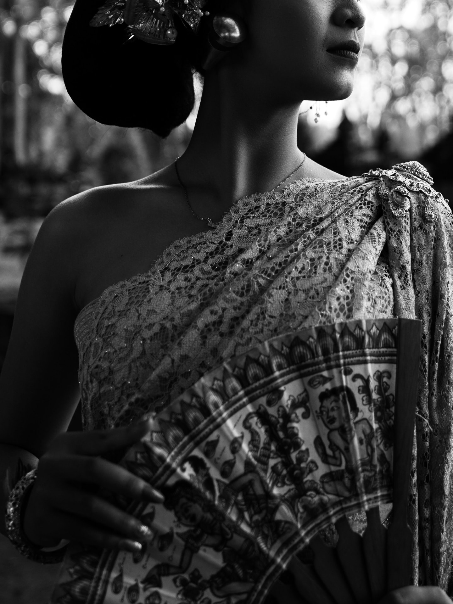 Black and white portrait of a Balinese dancer in traditional lace kebaya holding a painted fan