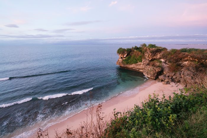 Pink dusk light over an empty Uluwatu beach and headland