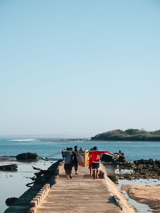 Men carrying a traditional boat along a stone pier