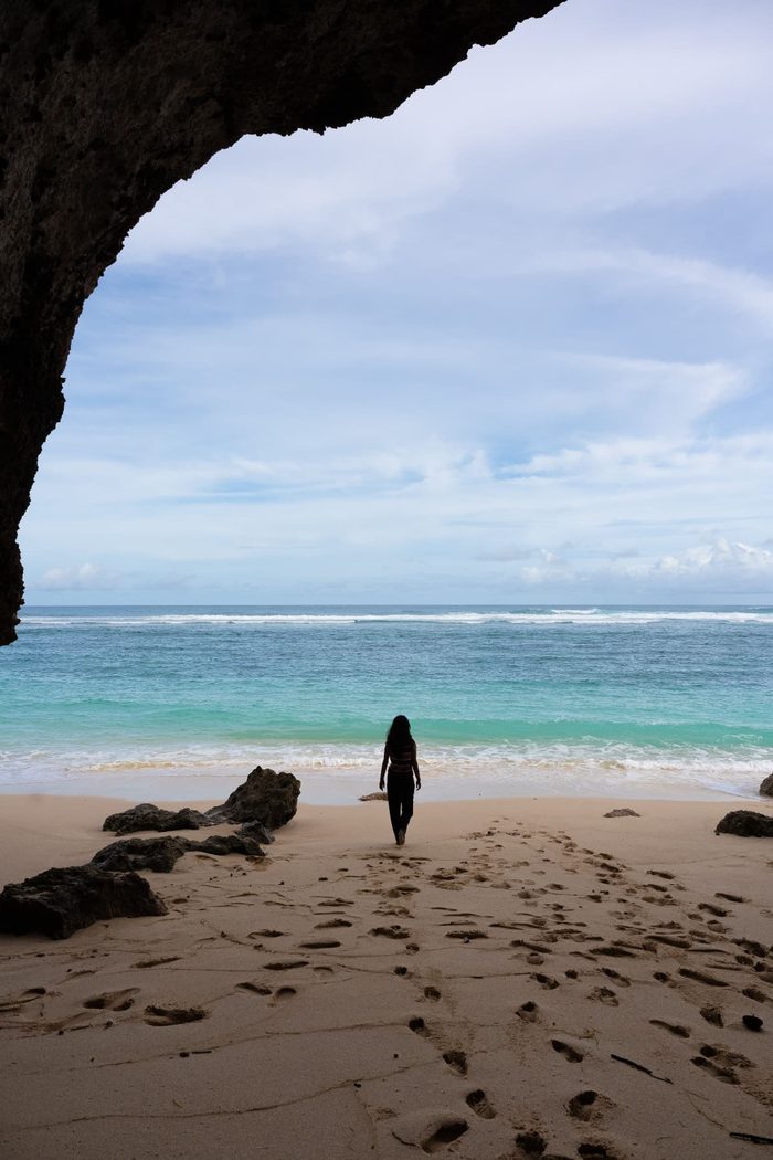 Person walking out of a limestone cave onto an Uluwatu beach