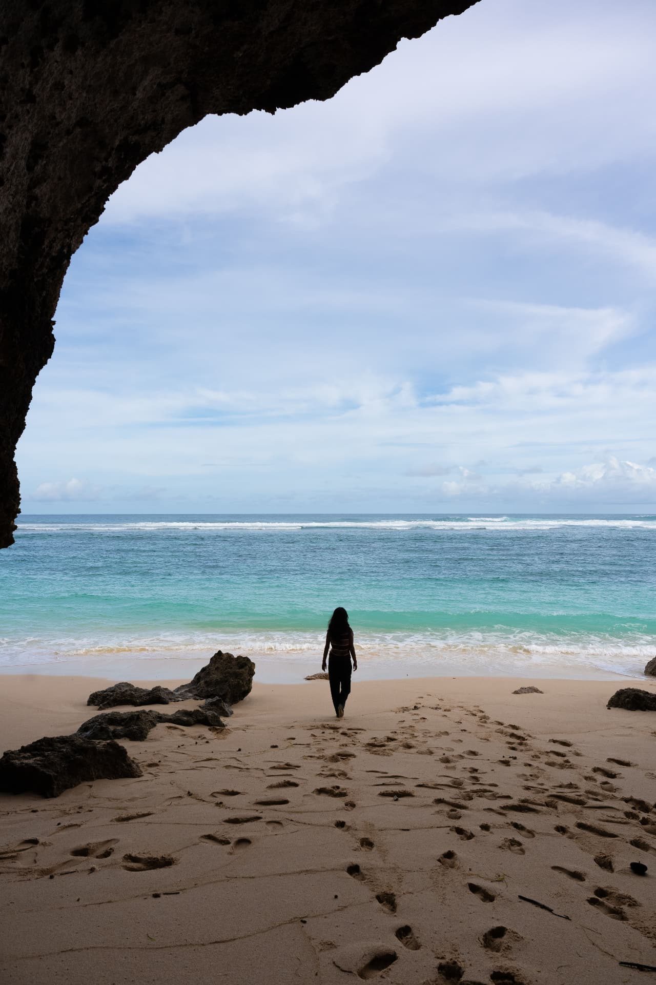 Person walking out of a limestone cave onto an Uluwatu beach
