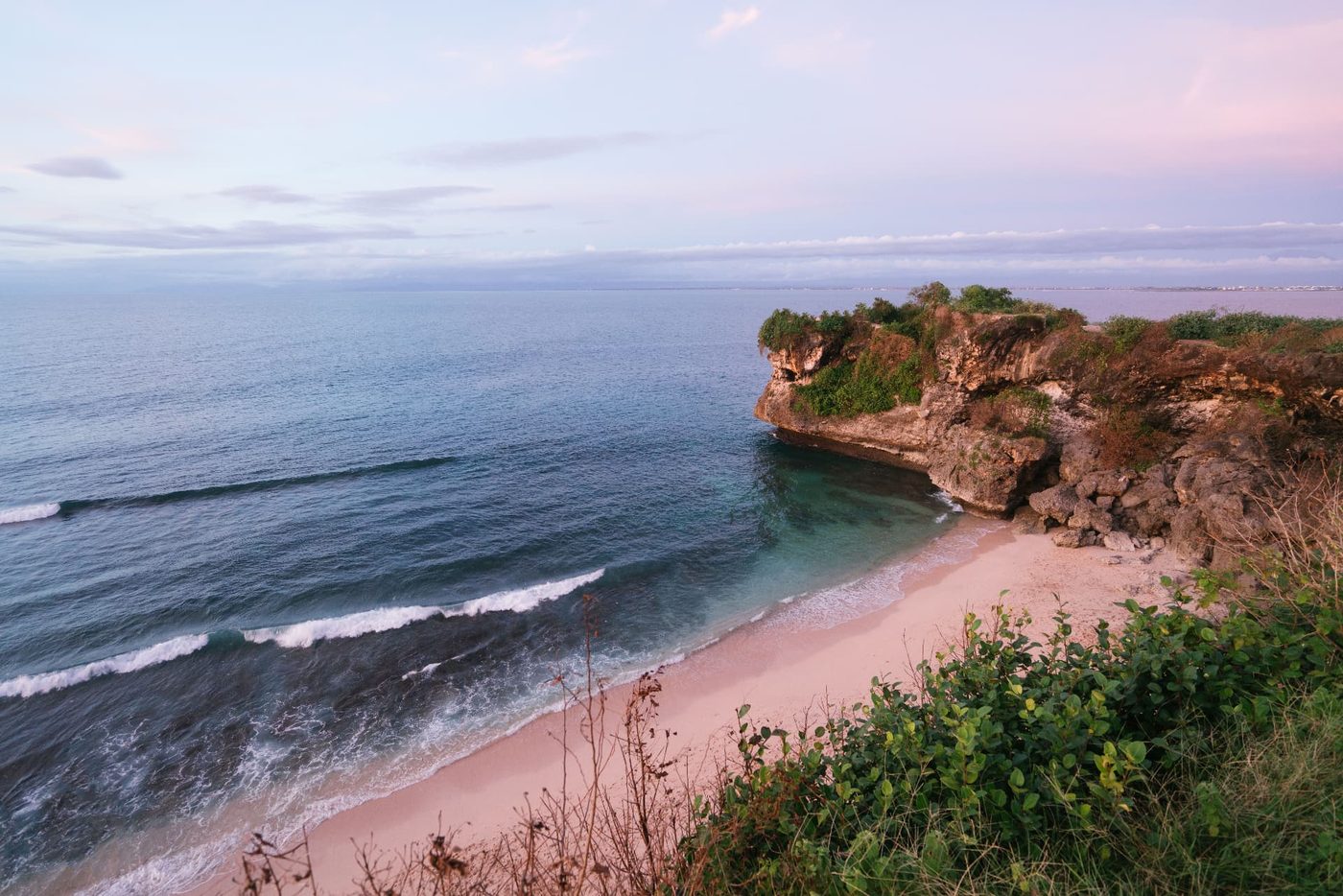 Pink dusk light over an empty Uluwatu beach and headland