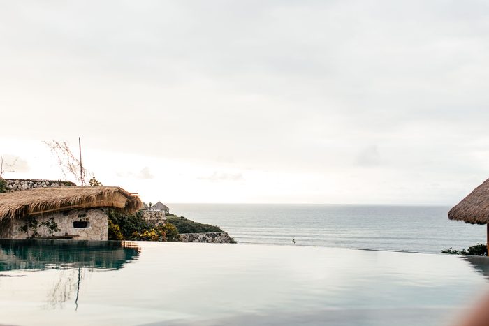 Infinity pool blending into the ocean beside a thatched cliff villa