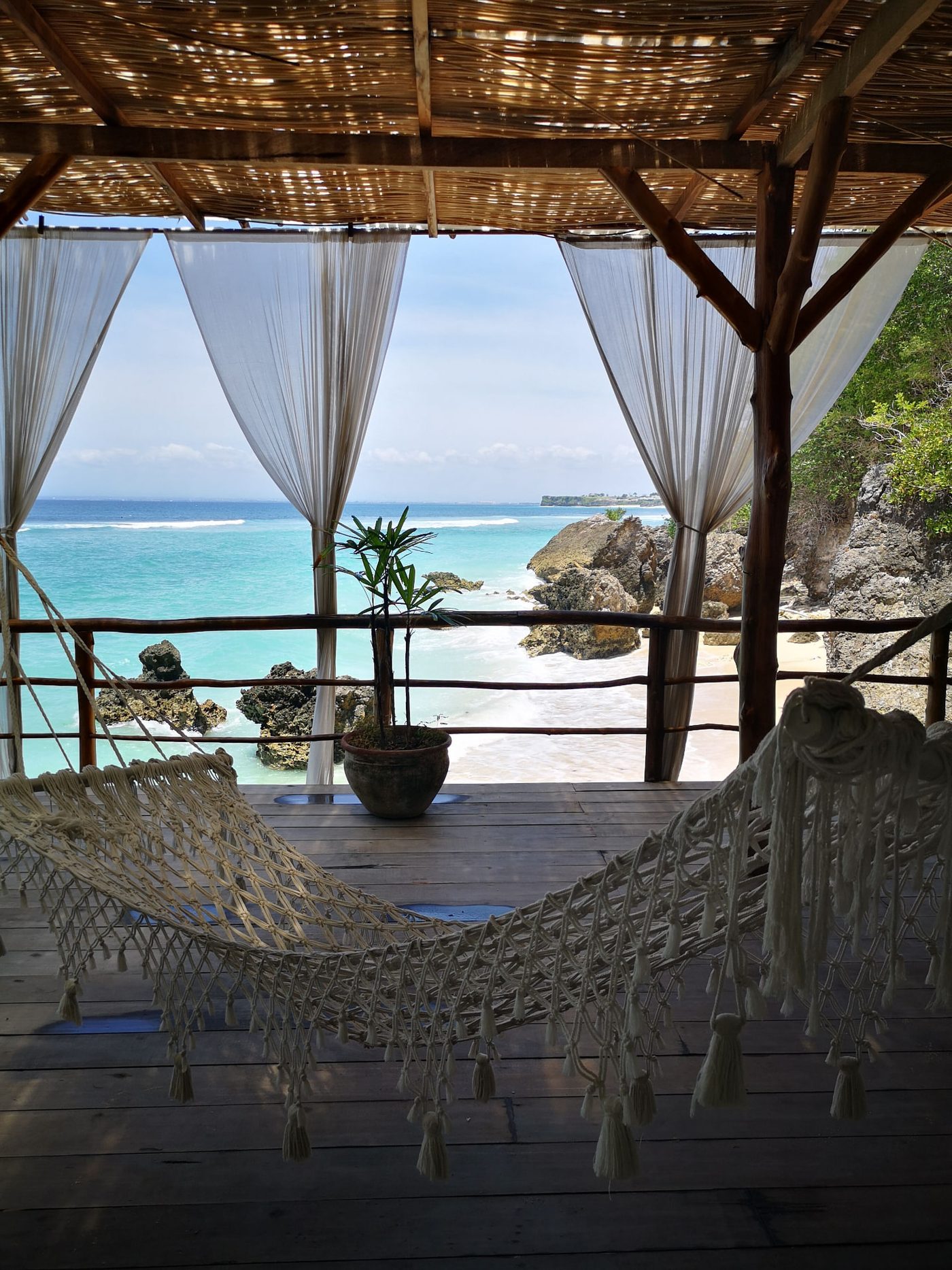 Hammock under a thatched shelter looking out to a turquoise Bali beach