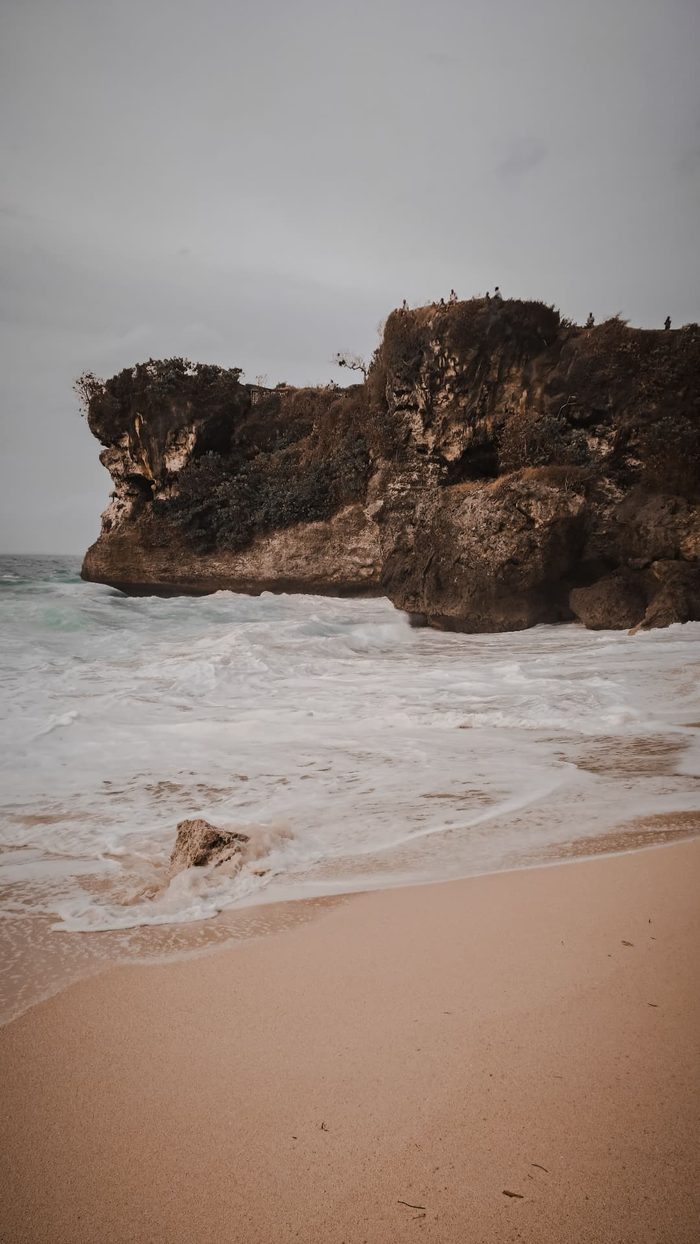 Waves washing the sand beneath an Uluwatu cliff on a moody day