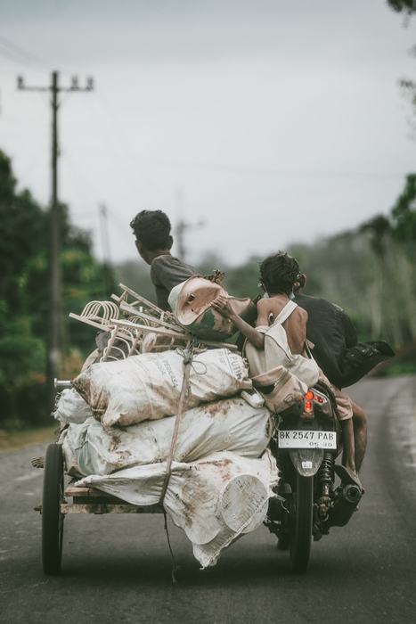 Men riding a loaded cart motorbike along a wet road